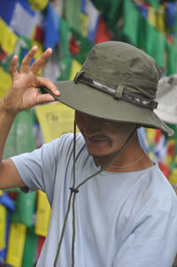 A happy asian young man looking down with touching hat, posing against tibetan prayer flags