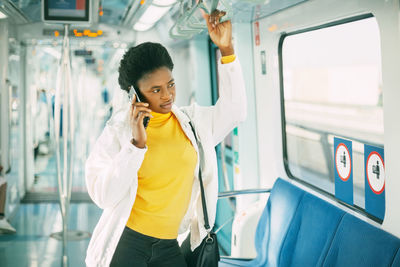 Full length of man using mobile phone while standing in bus