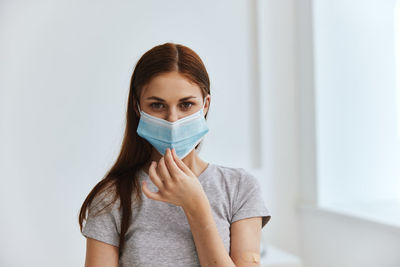 Portrait of young woman wearing mask while standing against wall