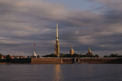 View of buildings by river against cloudy sky