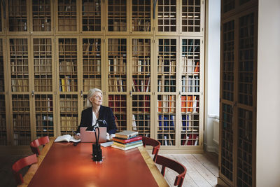 Senior professional looking away while sitting at table in law library