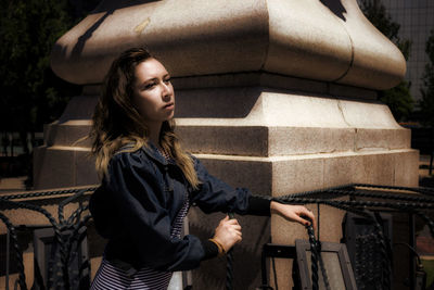 Young woman looking away while standing by column in city