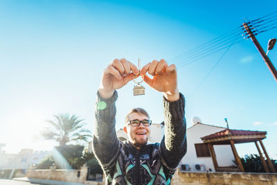 Portrait of young man with arms raised against sky