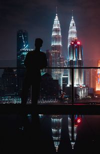 Rear view of man looking at illuminated city buildings
