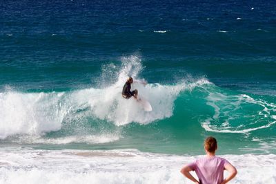 Man looking at surfer surfing in sea