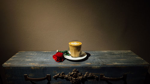 Red rose by latte on table against wall