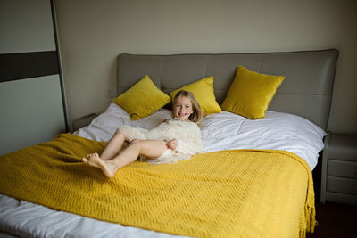 Beautiful little girl in stylish dress jumping on the bed with white blanket at home. stay at home 