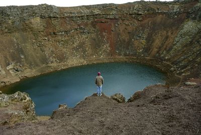 Rear view of man standing on rock by lake