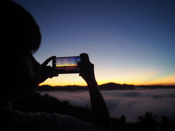 Cropped hand photographing sunset with mobile phone 