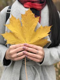 Midsection of woman holding maple leaf during autumn