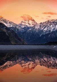 Scenic view of lake by snow covered mountains against sky during sunset
