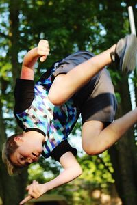 Tilt image of teenage boy jumping against trees