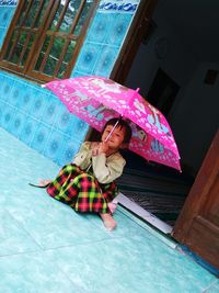 Portrait of girl holding umbrella while sitting at doorway