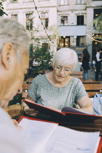 Senior man and woman reading menu while sitting at restaurant in city