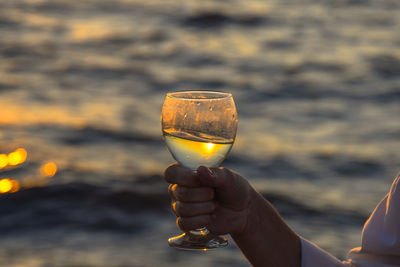 Close-up of hand holding drink against sky during sunset