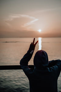 Rear view of silhouette man standing on sea against sky during sunset