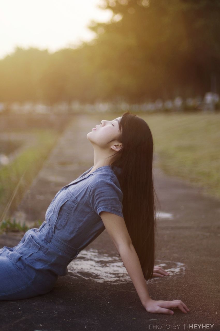 SIDE VIEW PORTRAIT OF SMILING YOUNG WOMAN AGAINST TREES