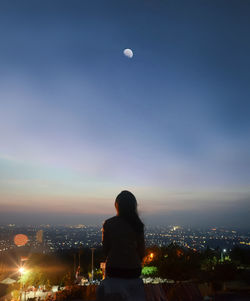 Rear view of woman enjoying view of illuminated buildings in city at night