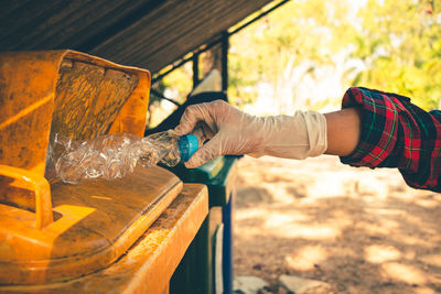 Cropped hand of person putting bottle in garbage bin