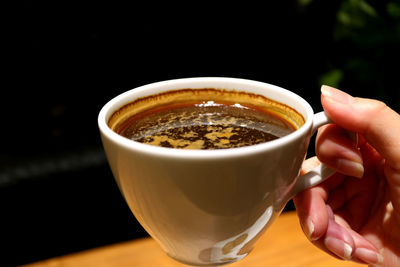 Female's hand holding a cup of hot coffee in the warm lighting dark room