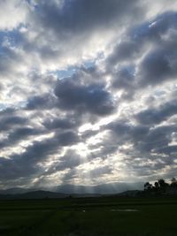 Sunlight streaming on field against sky during sunset