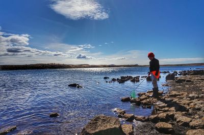 Girl fishing on shore against blue sky