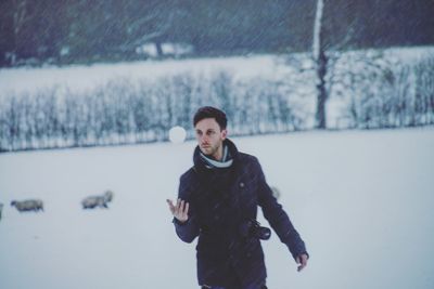 Man catching snow ball while standing on field