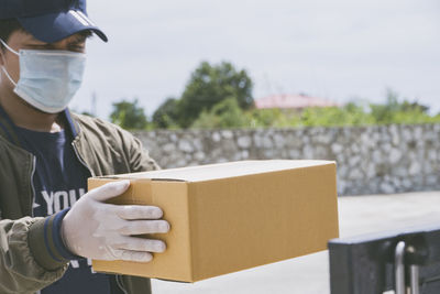 Delivery person wearing mask holding box standing outdoors