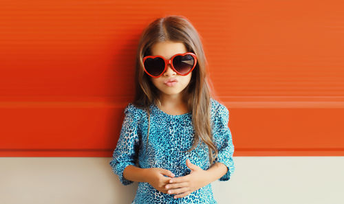 Portrait of young woman wearing sunglasses against yellow wall