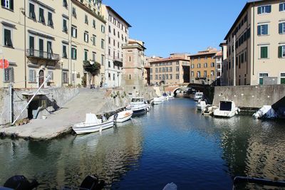 Boats moored in canal amidst buildings against clear blue sky