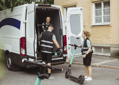 Female and male workers loading electric push scooters in delivery van