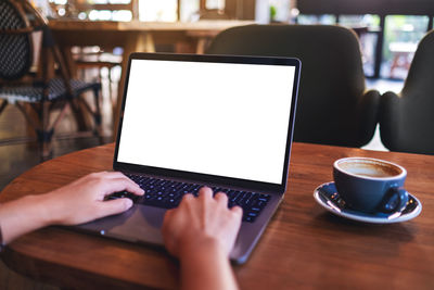 A woman using and typing on laptop computer keyboard with blank white desktop screen in cafe