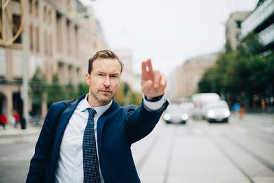 Portrait of confident mature businessman hailing taxi on street in city