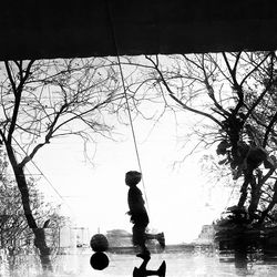 Side view of boy standing by bare tree against clear sky