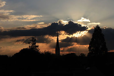 Silhouette of trees and building against cloudy sky