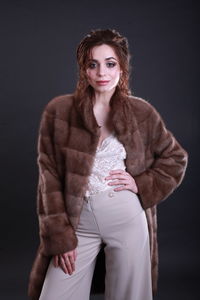 Fashionable young woman wearing fur jacket while standing against gray background