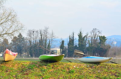 Boats moored on field by lake against sky