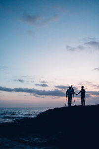 Silhouette people on beach against sky during sunset