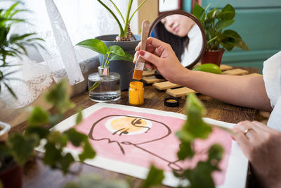 Closeup view of crop unrecognizable female artist creating picture with paint and brush on canvas in workshop