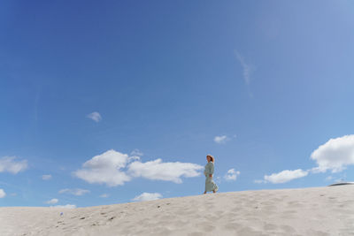 Rear view of man walking on beach against blue sky