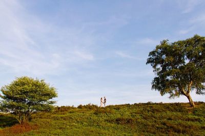 Mid distance of man and woman standing on grassy field against sky