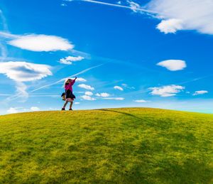 Low angle view of girl pointing while walking on hill against blue sky