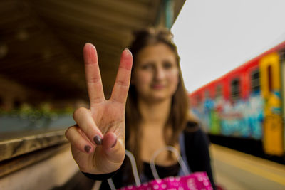 Close-up of woman gesturing peace sign while standing at railroad station