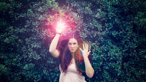 Beautiful young woman with arms raised standing against plants