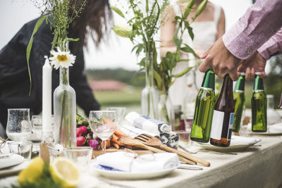 Cropped image of man holding beer bottles at dining table during dinner party in backyard