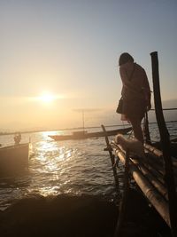 Man standing on sea against sky during sunset