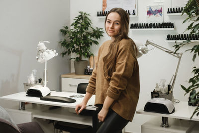 Nail service master. portrait of professional young brunette sitting at modern nail salon workplace