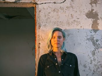 Young woman with closed eyes standing against wall