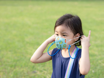 Portrait cute baby asian girl, little child with worried expression takes off protective face mask.