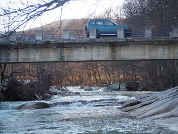 Bridge over river against buildings during winter